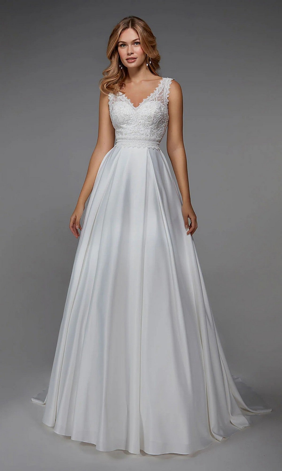 A woman models the Alyce 7035 Long White Dress in Diamond White, featuring a sleeveless lace bodice and flowing satin A-line skirt, standing before a plain gray background.